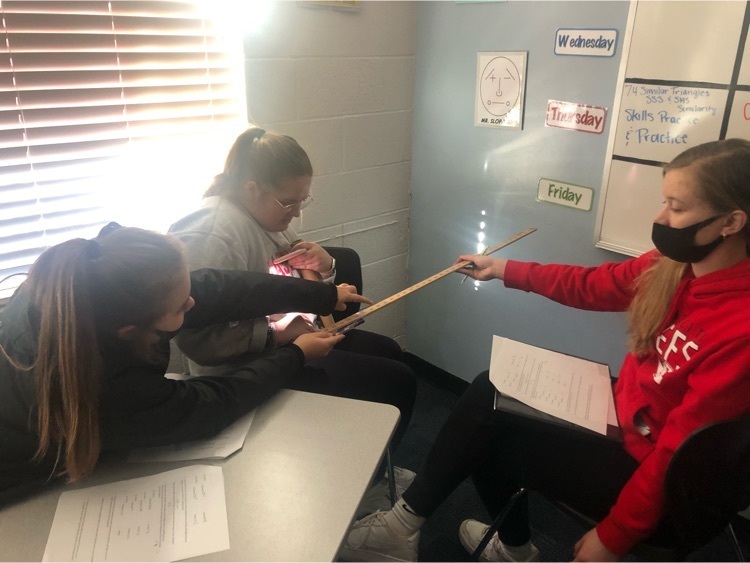 Geometry students using similar figures to estimate light projections on the wall.